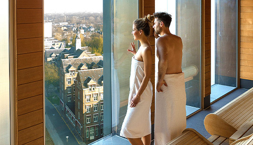 Stel kijkt uit het raam bij de panoramasauna bij BLUE Wellnessresort Leiden